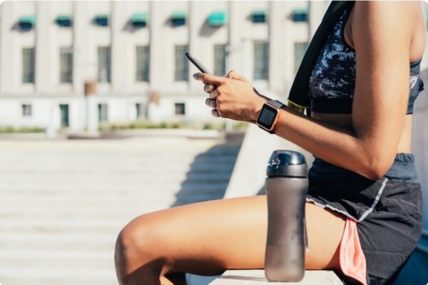 marathon runner diet - woman sitting on a bench with a fluid bottle in a running break