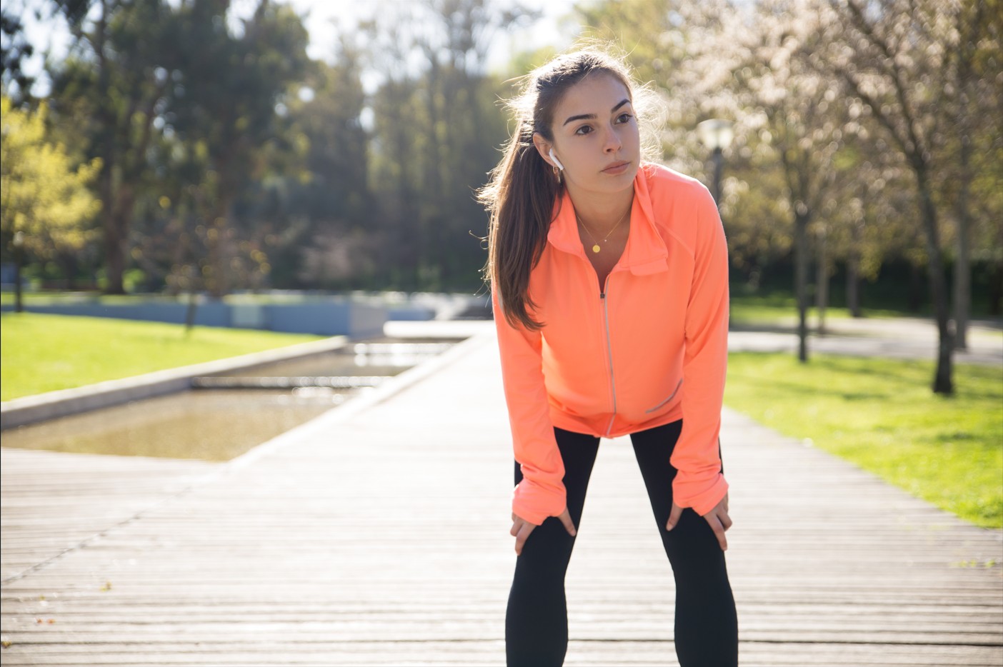 Endurance training - Woman runner in morning light with hands on knees, catching breath