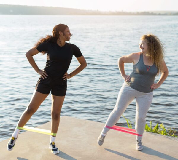 Two women exercising with resistance bands outdoors by the wate