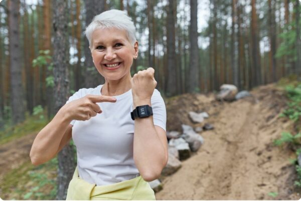 training zones - Happy fit retired female in activewear smiling broadly pointing at display of her wrist smart watch